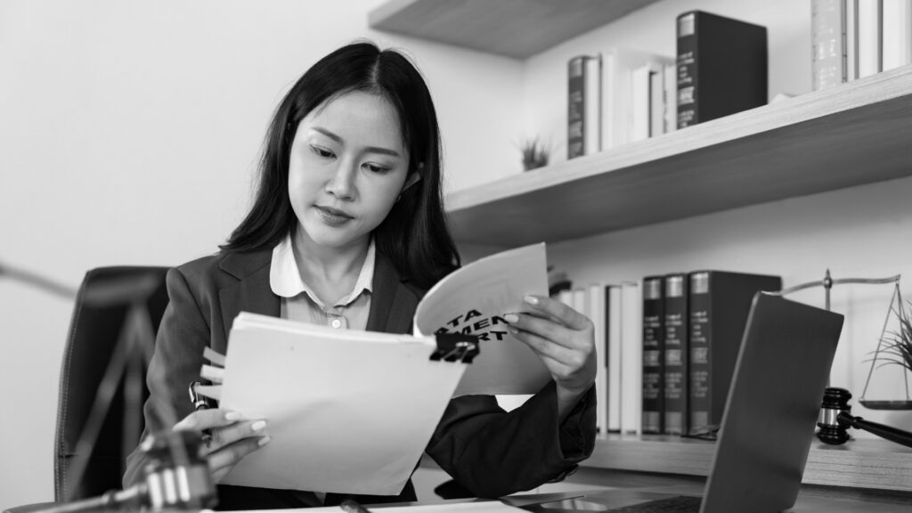 Legal Assistant seated at a desk reviewing legal documents, with law books and a gavel visible in the background.